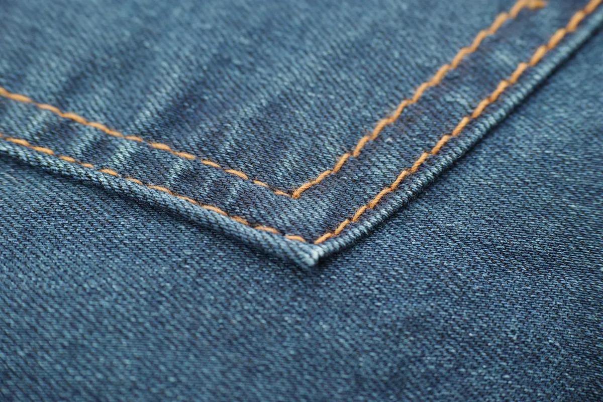 Jean brut en denim indigo posé sur une chaise, patine visible aux plis